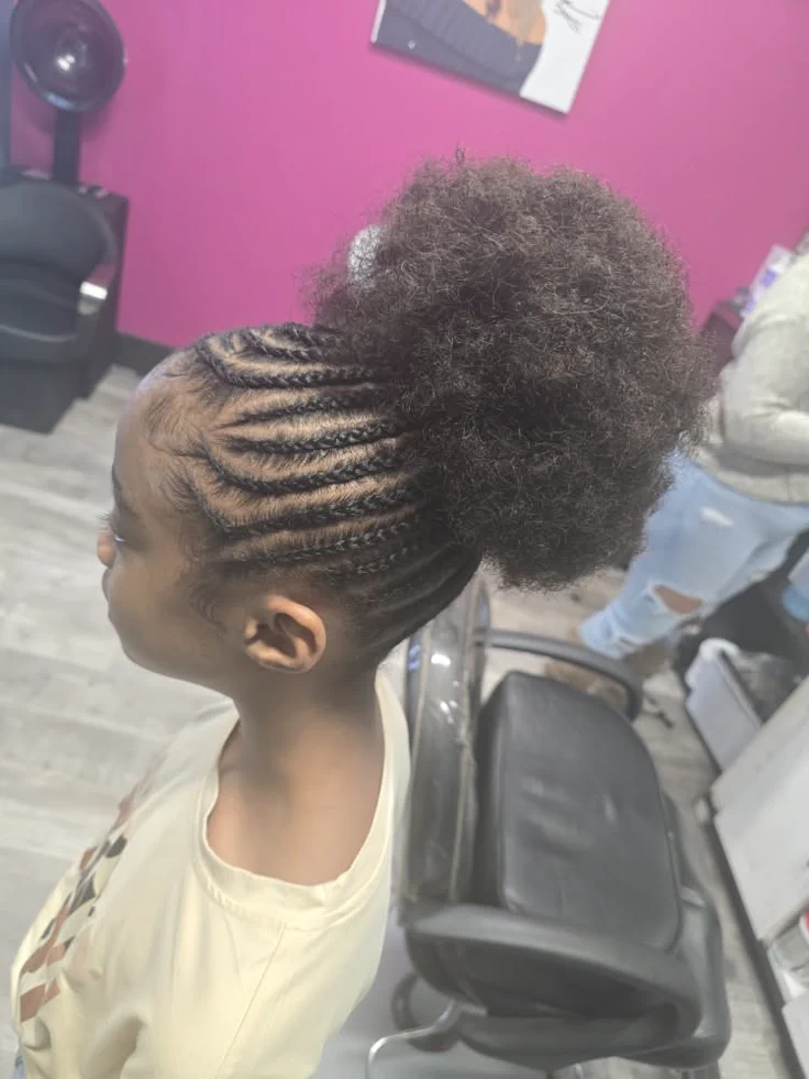 A child wears small braids framing the hairline, feeding into a high, full natural puff.