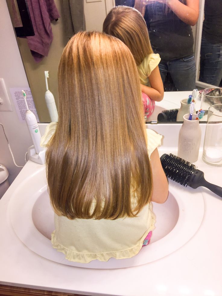 Back view of a child's long, straight hair leaning over a bathroom sink, showing smooth, sleek strands from root to tip.