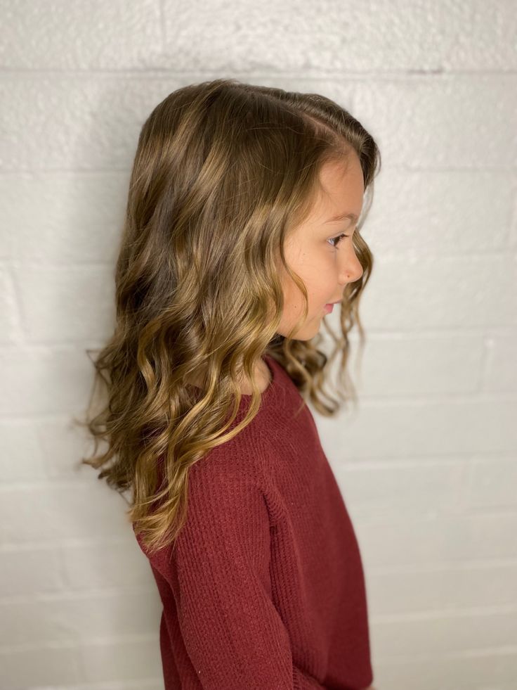 Young girl with type 2C wavy hair walking outdoors near flowering hydrangea bushes, curls loose near the roots and more defined toward the ends.