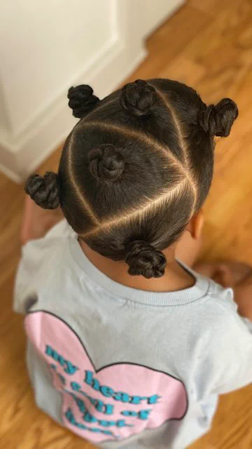 young girl with bantu knots with her back facing the camera showing the triangular parting