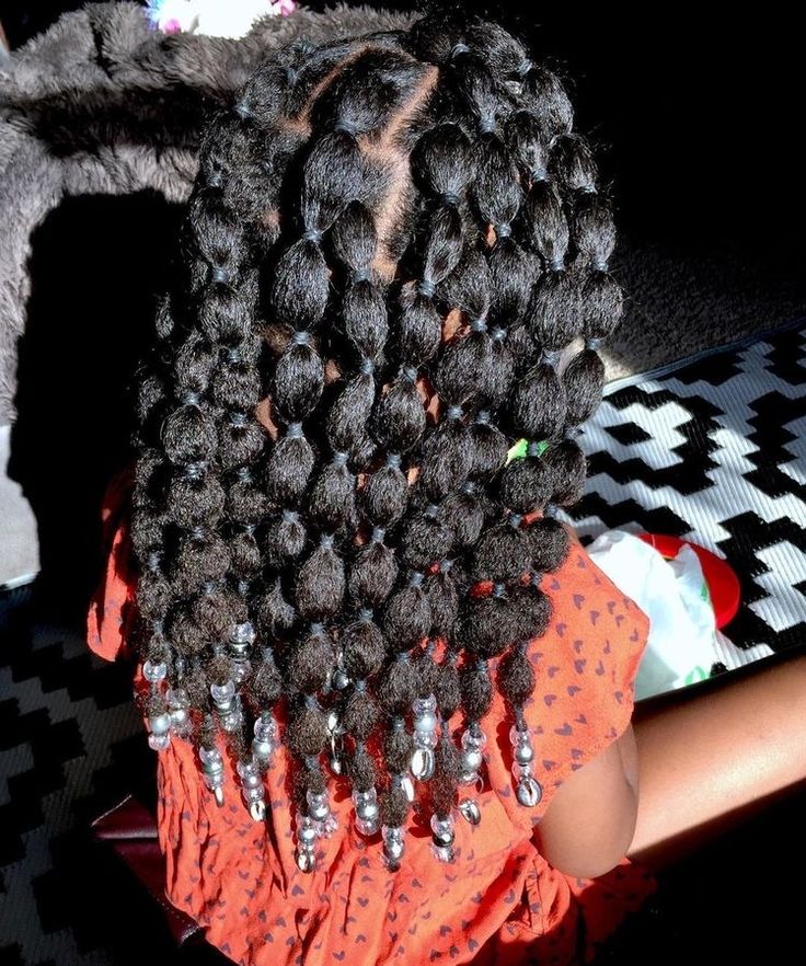 A child's hair is styled in bubble box braids with small elastics creating a textured effect, finished with silver beads.
