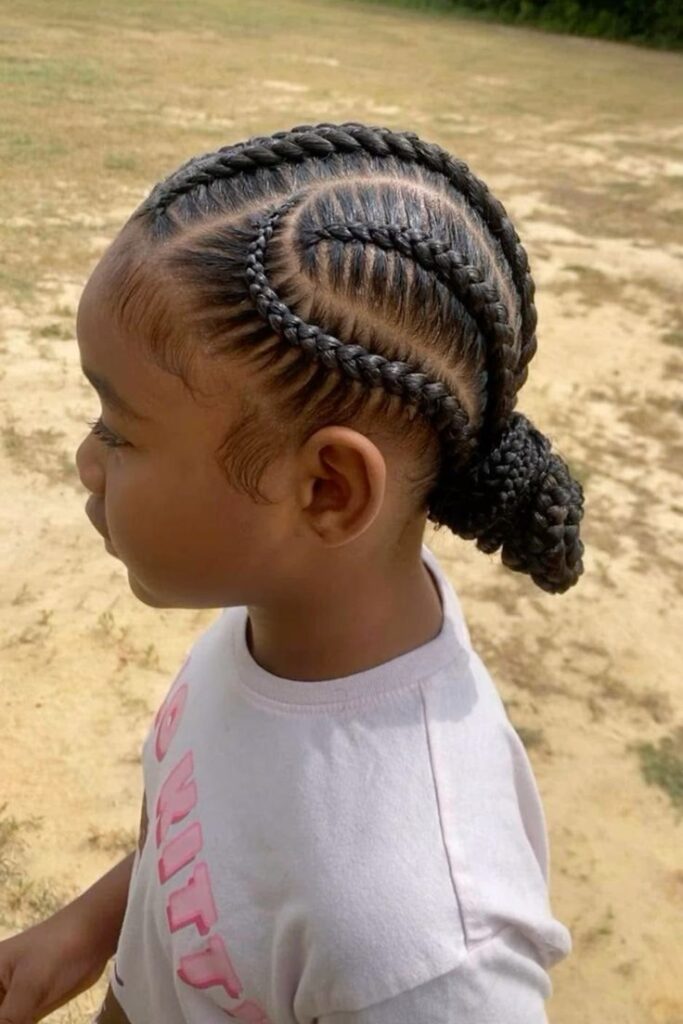 Side view of a child with swirl-pattern cornrows gathering into a low braided bun.