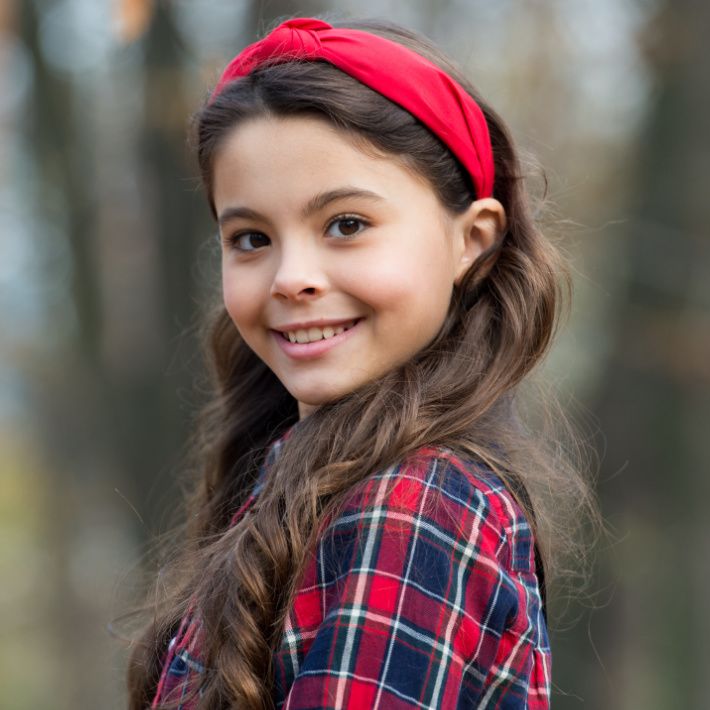 Smiling girl wear knotted headband. Biggest Hair Accessory Trends. Adorable little girl checkered shirt wear red headband.