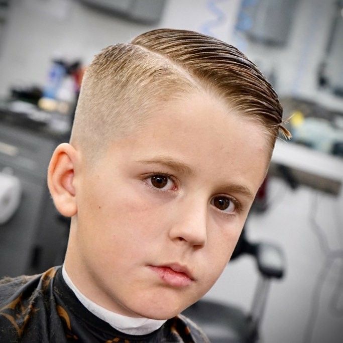 Close-up of a young boy with an Ivy League haircut, hair combed back with a defined side part on top, blending into a tapered fade on the sides.