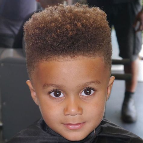 Close-up of a young boy with a high-top afro haircut, a tall, flat-topped shape of dense coily hair blending into a fade on the sides.