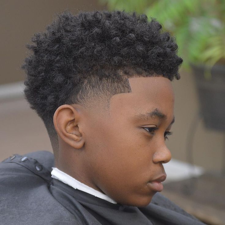 Side profile close-up of a young boy with a temple fade haircut, curly hair on top with a fade concentrated around the temple and a sharp line-up.