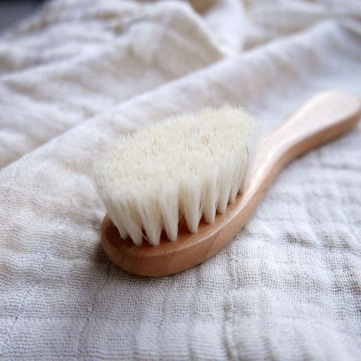 A soft-bristle wooden baby brush resting on a folded linen cloth."