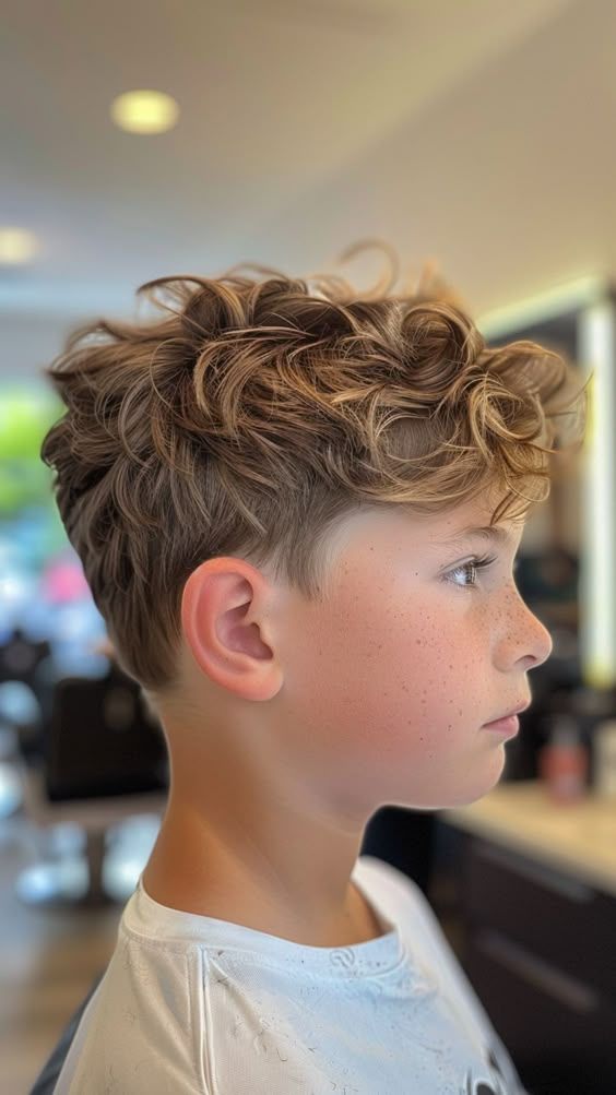 Side profile close-up of a young boy with a curly shag haircut, loose layered curls with movement on top blending into tapered sides.