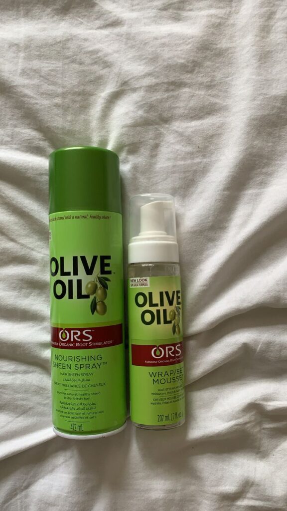 Bottles of ORS Olive Oil Nourishing Sheen Spray and Olive Oil Wrap/Set Mousse styling products for hair.