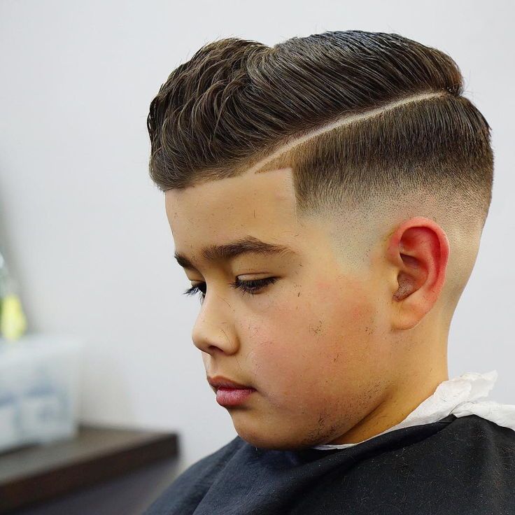 Side profile close-up of a young boy with a side part haircut, hair combed to one side with a sharp, defined part line, blending into a faded side.