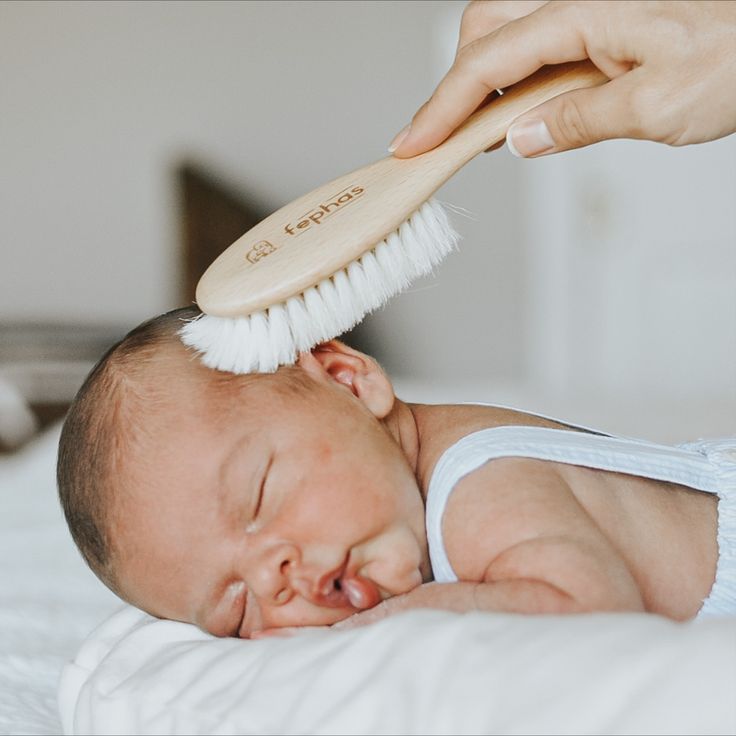 A hand brushing a new born scalp to remove cradle cap