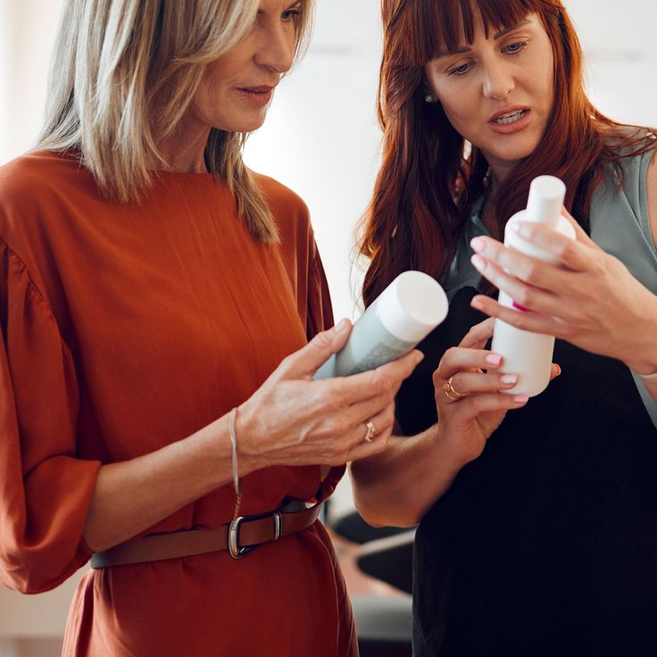 Two women discussing hair product bottles together, one appearing to give advice