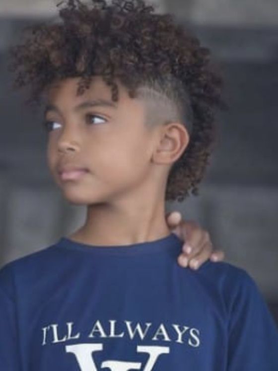 Side profile of a young boy with a Frohawk haircut, curly hair styled fuller through the center, blending into a faded side.