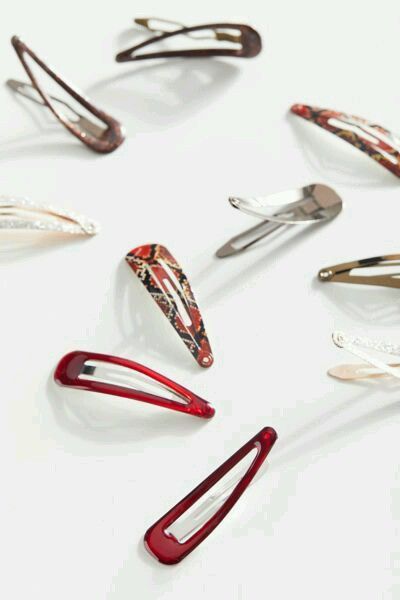 Assorted metal and patterned snap hair clips scattered on a white background, showing their smooth curved edges