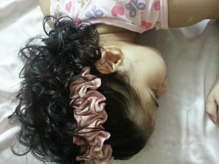 Overhead view of a young girl asleep on a pillow with a satin scrunchie still tied in her curly dark hair.