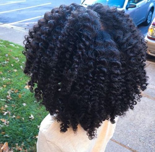 Back view of thick, defined natural curls resting past the shoulders outdoors
