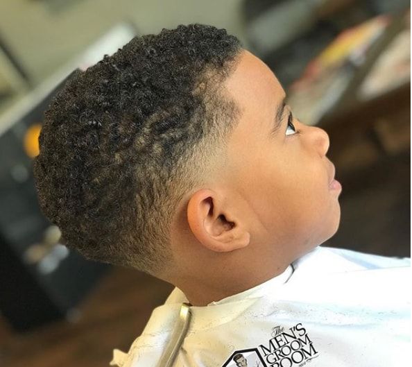 Side profile close-up of a young boy with a temple fade with curls haircut, coily curly hair on top blending into a fade concentrated around the temple.