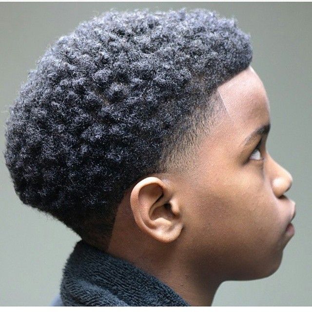 Side profile close-up of a young boy with a tapered afro haircut, shorter tapered sides blending into a fuller, rounded coily top.