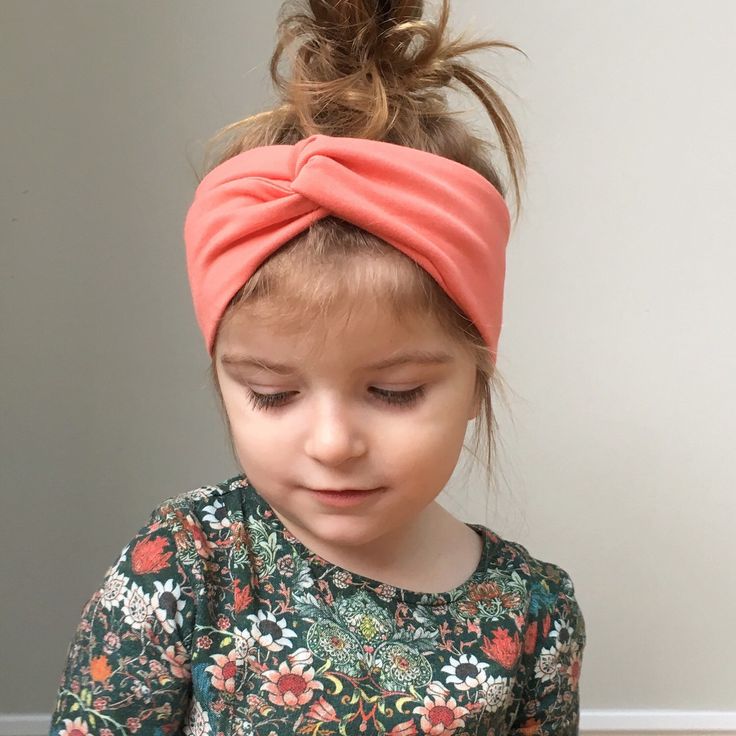 Young girl wearing a soft coral knotted fabric headband with her hair loosely gathered in a high bun