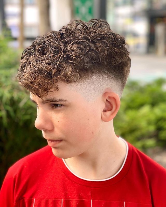 Side profile close-up of a young boy with a long curly top haircut, full, defined curls left long on top blending into a fade on the sides.