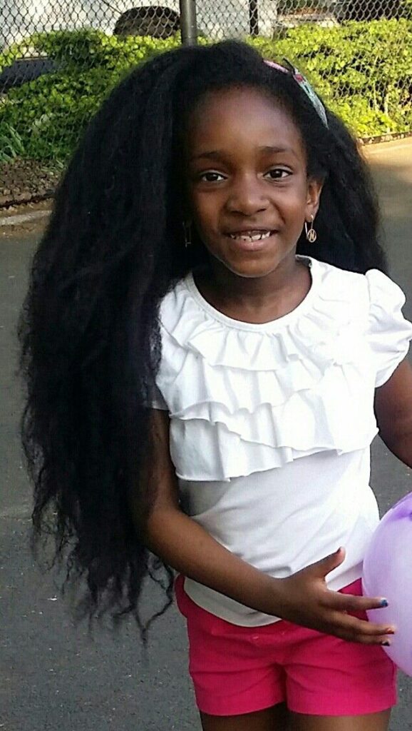 A smiling girl outdoors with long, healthy natural hair reaching well past her waist.