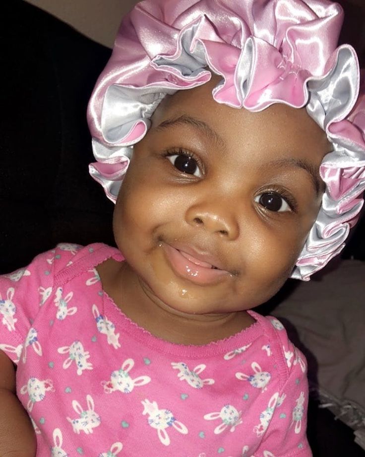 Baby girl wearing a pink satin bonnet with ruffled edges to protect her hair at night.