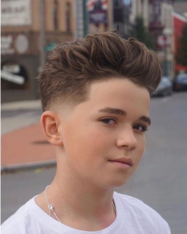Close-up of a young boy with a textured quiff haircut, voluminous, lifted hair pushed up and back on top, blending into a fade on the sides.