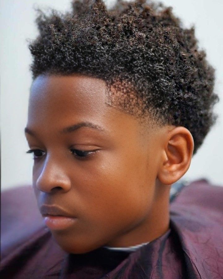 Side profile close-up of a young boy with a shaped afro haircut, coily hair trimmed into a defined, sharp outline near the hairline.