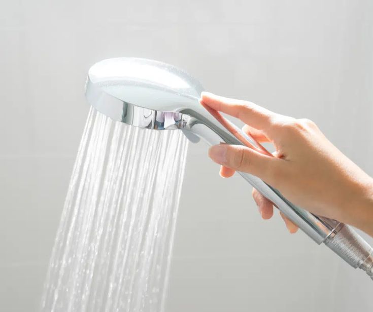 Hand holding a chrome handheld showerhead with water spraying out."