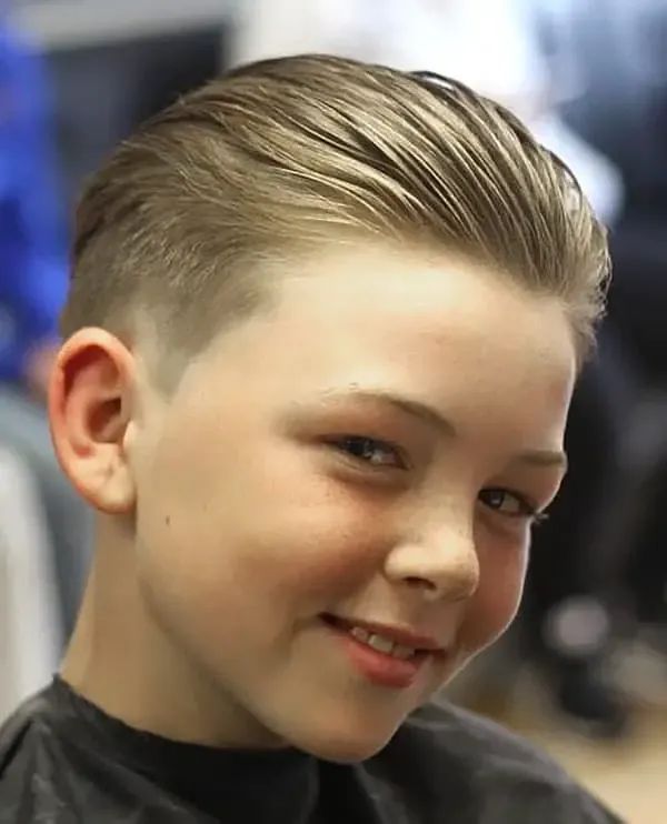 Close-up of a young boy smiling, hair styled in a slick back with all the top hair combed straight back for a sleek, polished finish.
