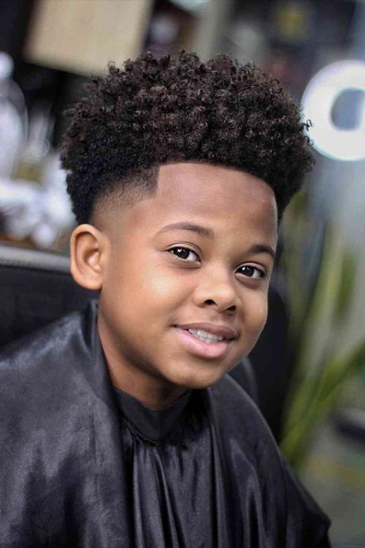 Close-up of a young boy smiling, hair styled in a blowout fade with voluminous, blown-out curly hair on top and a clean fade on the sides.
