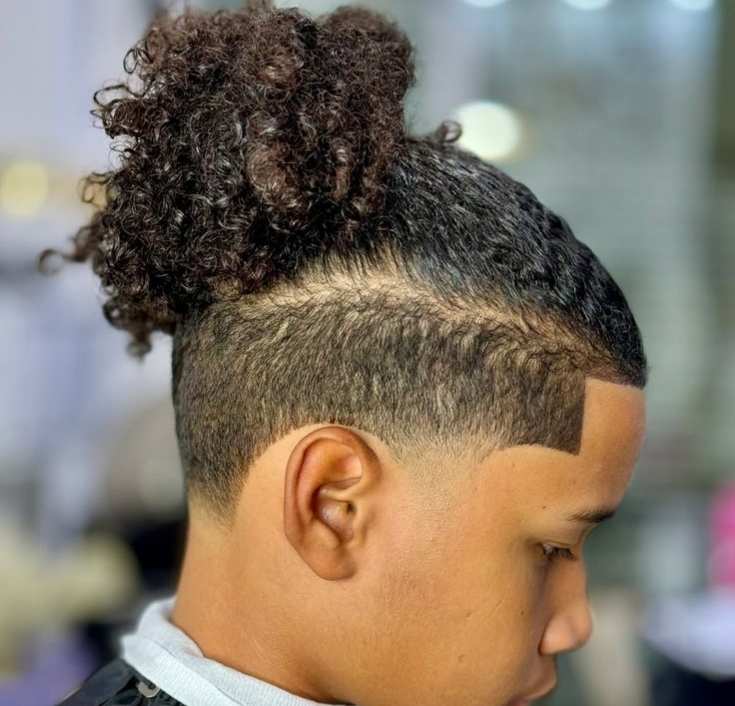 Side view of a boy with a curly top knot bun and a shaved-line undercut fade on the sides.