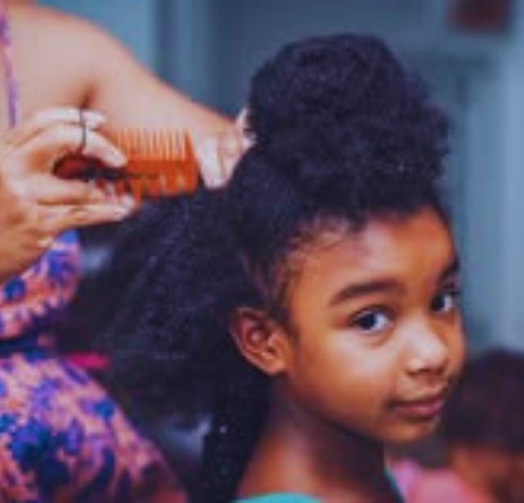 A young girl sitting quietly while her her is being detangled for styling showing no discomfort