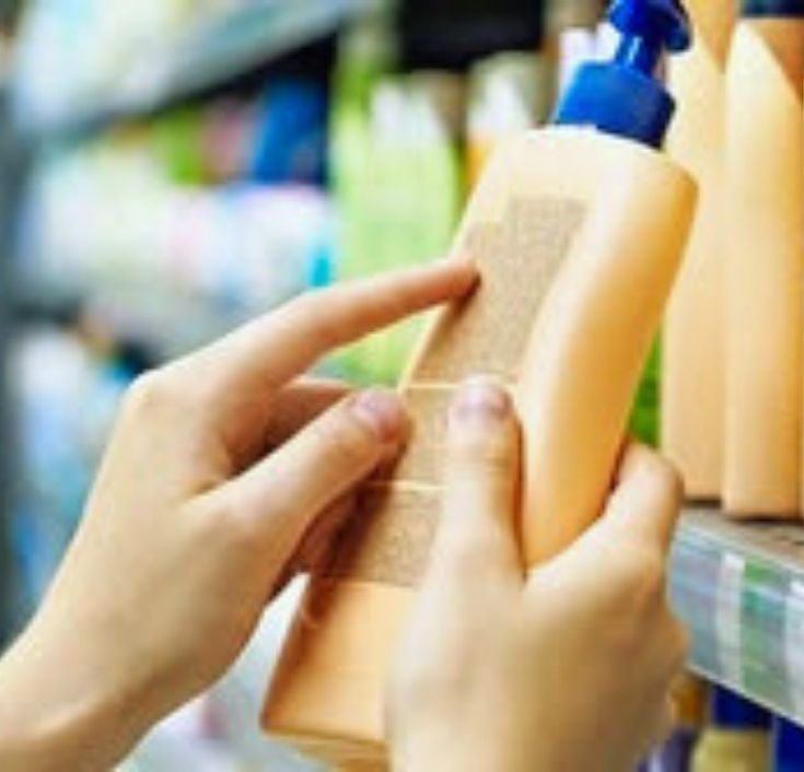 Close-up of a hand pointing to the ingredient label on a hair product bottle in a store."