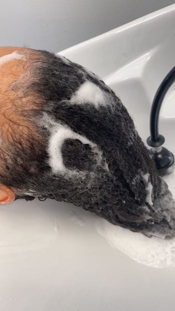 Long, saturated hair being combed through during rinsing, illustrating how thorough detangling helps water reach every section evenly to fully remove product."