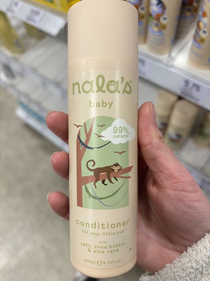 A hand holding a bottle of Nala's Baby Conditioner made with oats, shea butter, and aloe vera, in a store aisle."
