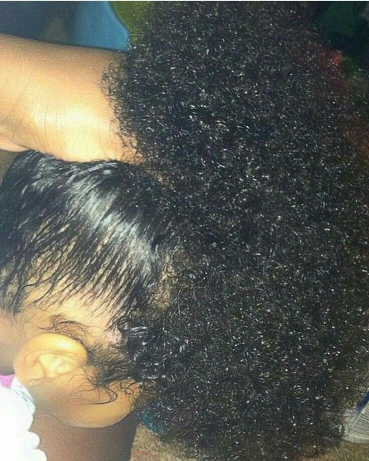 A hand lifting a section of a toddler's thick, curly hair, showing volume and length at the crown."