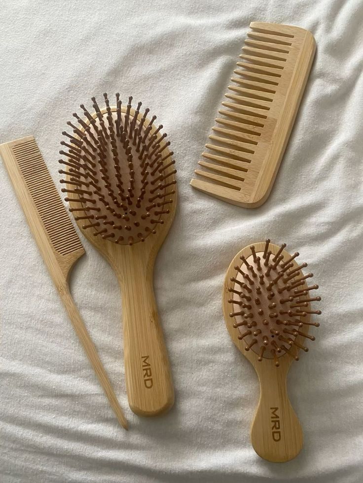 "A set of wooden hair care tools laid on a bed, including a wide-tooth comb, rat-tail comb, and two soft-bristle paddle brushes."