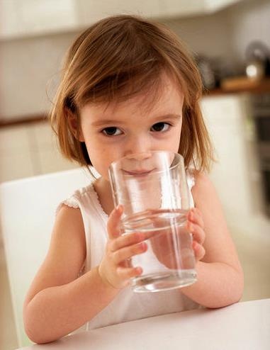 A young child drinking a glass of water at a kitchen table."
