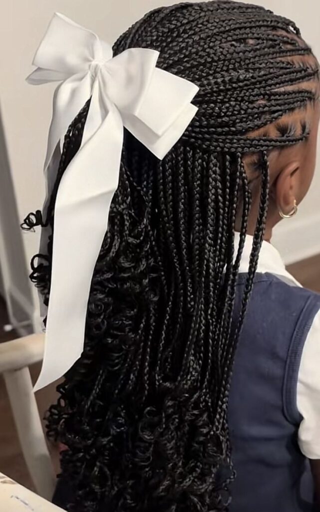 Child wearing half up styled  knotless braids with curly ends and a white bow