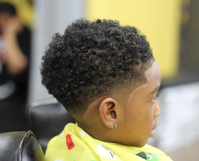 Side and back view of a young boy with a drop fade haircut, curly hair on top and a fade that curves downward and around the ear.