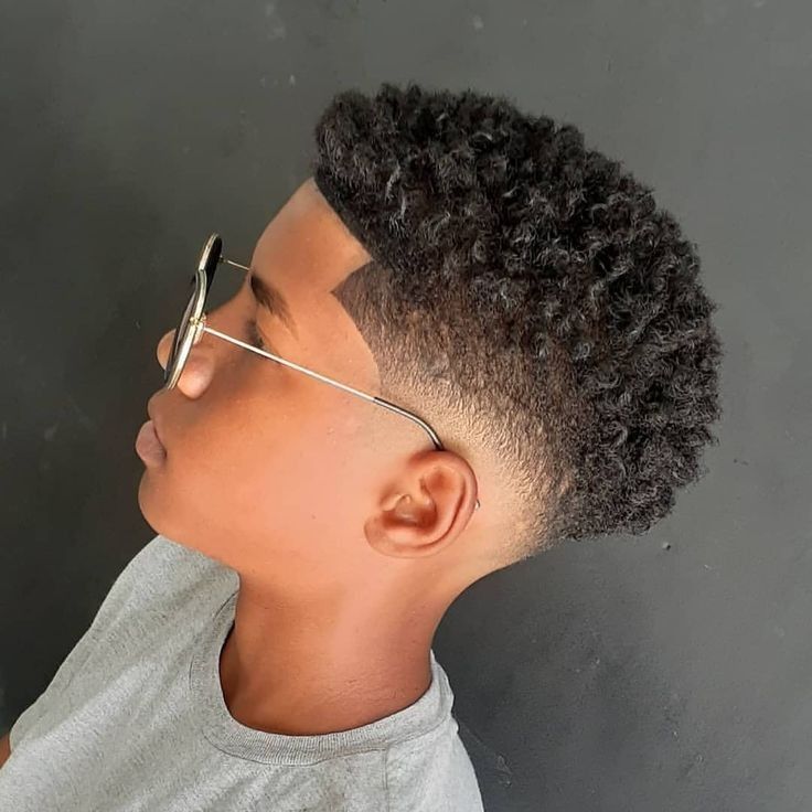 Side profile close-up of a young boy wearing glasses, hair styled with a skin fade tapering to bare skin on the sides and curly texture left on top.