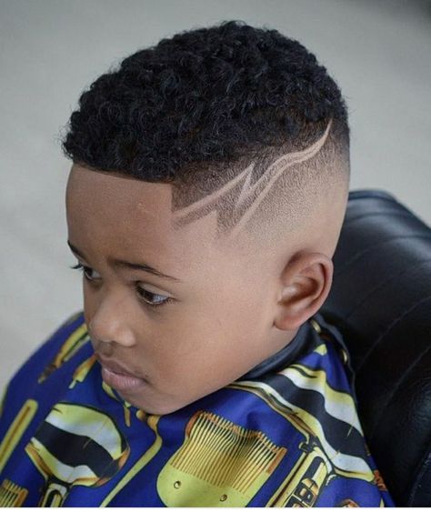 Side profile close-up of a young boy with a fade haircut featuring a shaved-in line design, curly hair kept fuller on top.
