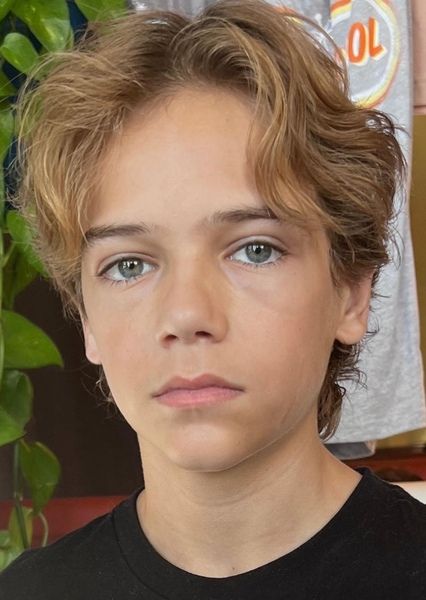 Close-up portrait of a young boy with a curtains haircut, hair parted down the center with both sides falling naturally over the forehead.