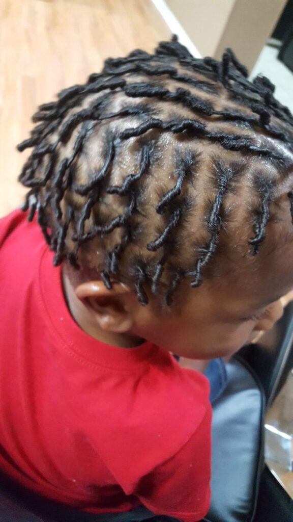 Top-down close-up of a young boy with short locs, short, rope-like locs sitting close to the scalp.
