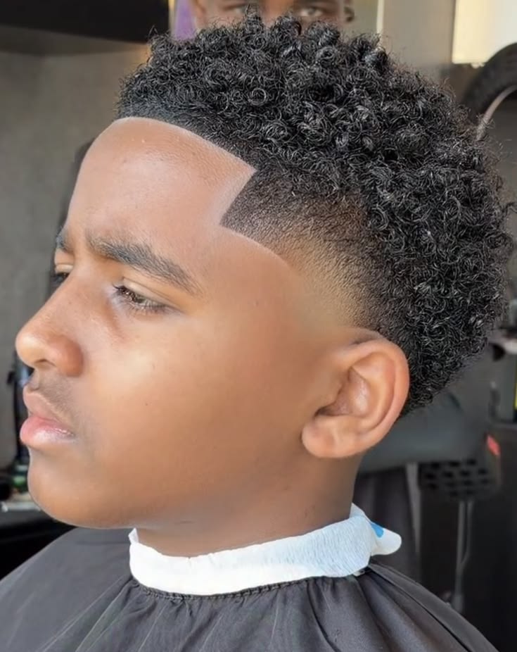Side profile close-up of a young boy with sponge curls, small, tightly defined coils on top blending into a fade with a shaved-in line design.