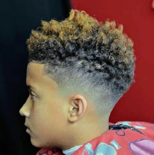 Side profile close-up of a young boy with a drop fade haircut, curly hair with lightened tips on top, blending into a fade that curves downward around the ear.