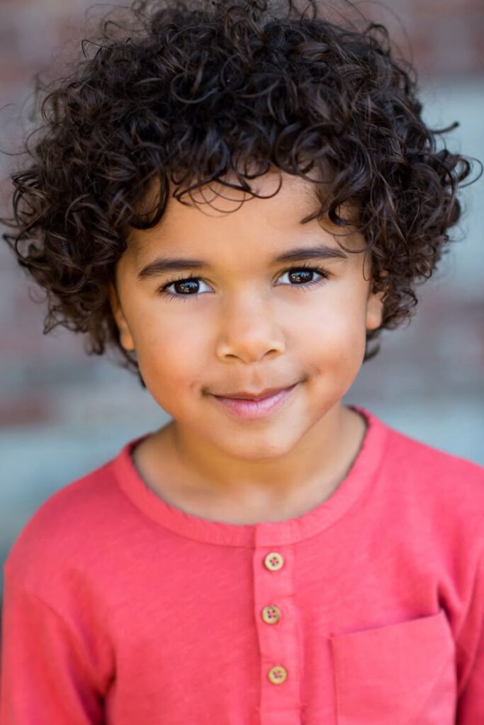 Close-up portrait of a young boy with evenly rounded curly hair styled as a curly bowl cut.