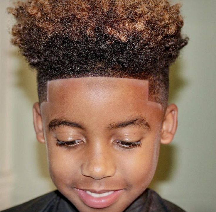 Close-up of a boy with tall, boxy curly volume on top with color highlights and a clean fade on the sides.