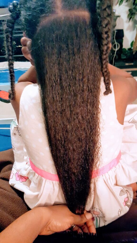 A hand holding a section of long, healthy hair stretched taut, showing natural elasticity and length.
